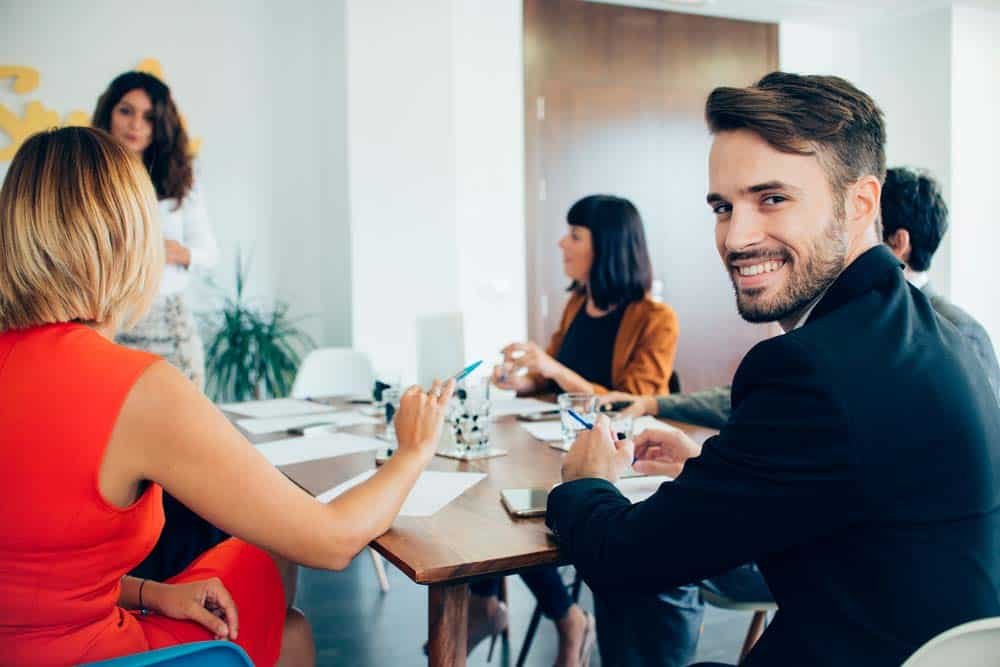 Business team in a meeting room with a smiling man looking back at the camera.