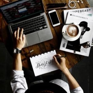 Overhead view of a designer's desk with a laptop, coffee, and sketching pad.