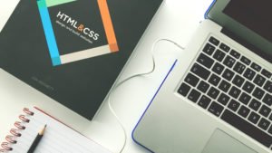 Web development programming book and laptop on a white desk surface.
