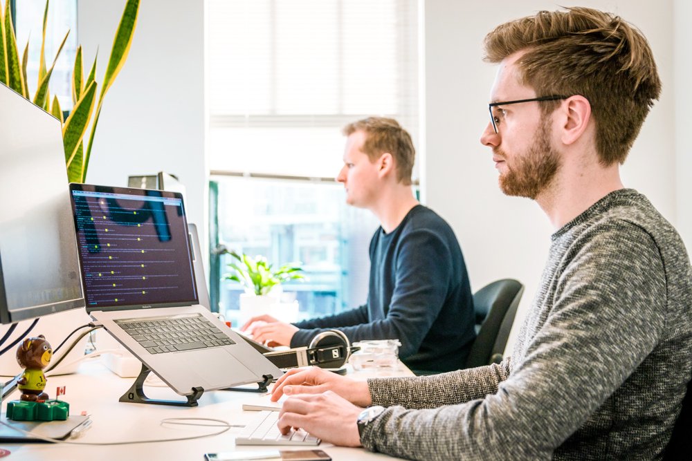Two developers working on laptops in a bright modern office.
