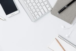Flat lay view of a modern desk with a keyboard, notebook, and pen.