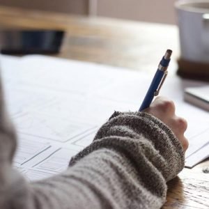 Person writing notes on paper at a wooden table.